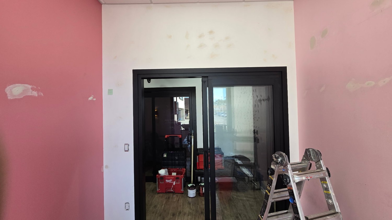 Room with a pink patched wall, ladder, and floor coverings