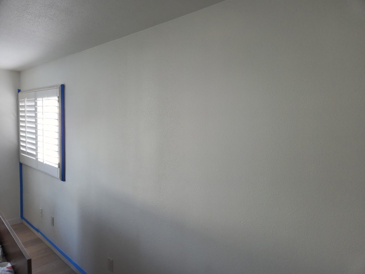 Light-colored interior wall beside a shuttered window with blue tape at the floor